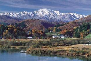 紅葉が残る里山の景色の後ろに雪化粧した飯豊山