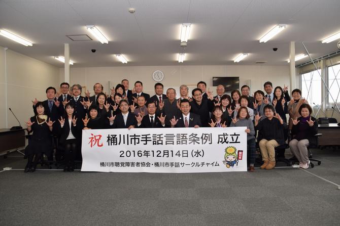 手話言語条例成立の横断幕を持って記念撮影する関係者の写真