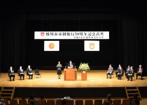 令和3年10月30日(土曜日)に執り行った「桶川市市制施行50周年記念式典」の様子の画像。演台を前に式辞を述べる小野桶川市長と来賓(大野元裕知事、岡地県議会副議長、原口和久鴻巣市長)、糸井政樹市議会議長が映っている。