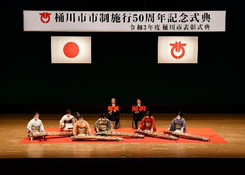 桶川市市制施行50周年記念式典で演奏を披露する桶川三曲協会の皆さんの画像。筝、三絃、尺八の奏者が六段の調を奏でている。