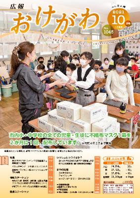 「市内小・中学校の全ての児童・生徒に不織布マスク1箱を2か月に1回、配布しています。令和4年2月まで実施」と書かれ、市内小学校のとあるクラスで先生からマスクを1箱受け取っている児童の様子が表紙となった広報おけがわ10月号の画像