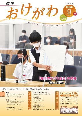 広報おけがわ9月号の表紙画像。子ども議会で女の子がクリップボードに印刷されたグラフを基に説明する様子が写っている。