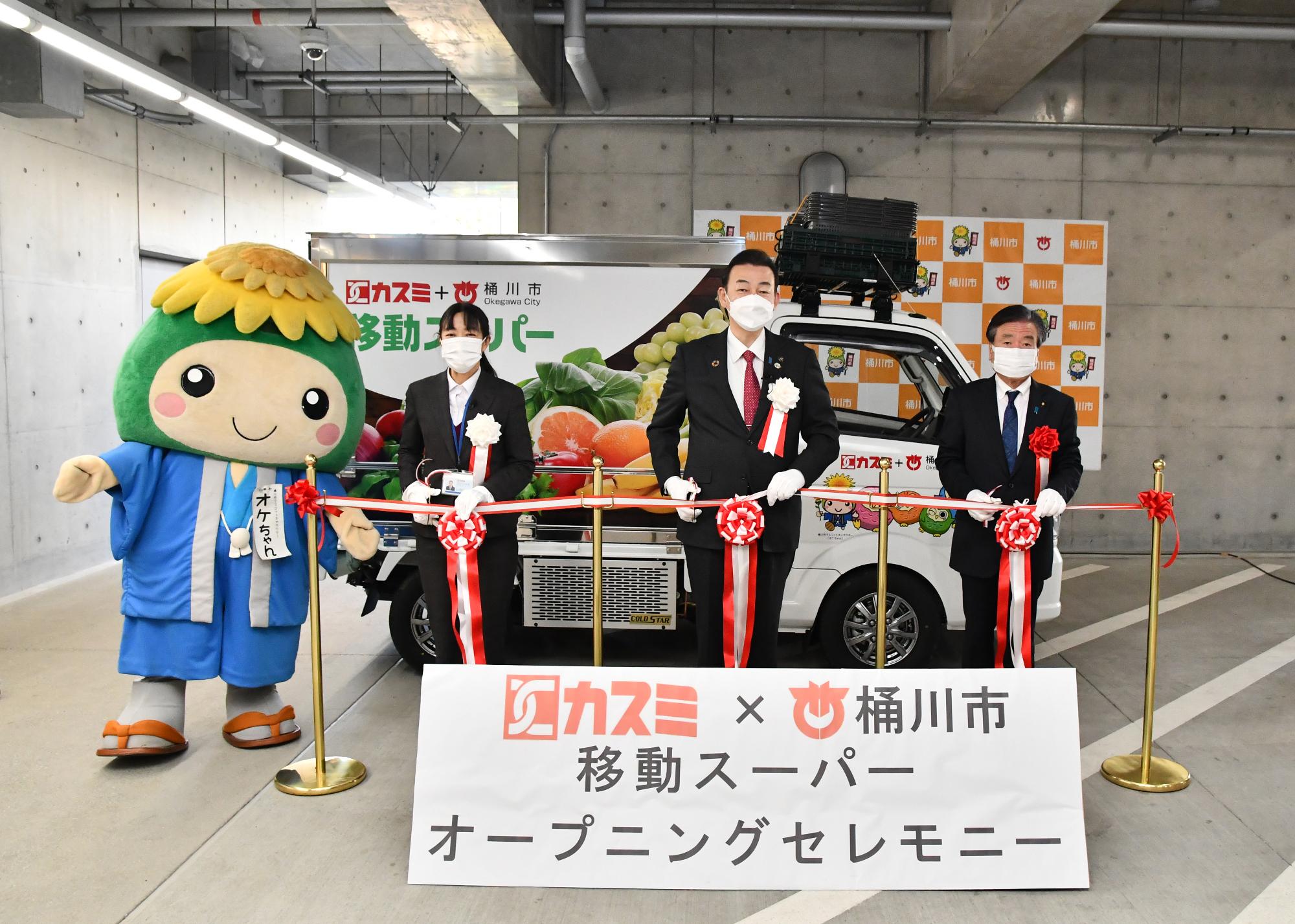 市役所1階のピロティ駐車場で行った「移動スーパー出発式」で、株式会社カスミのご担当者、桶川市長、テープカットの様子