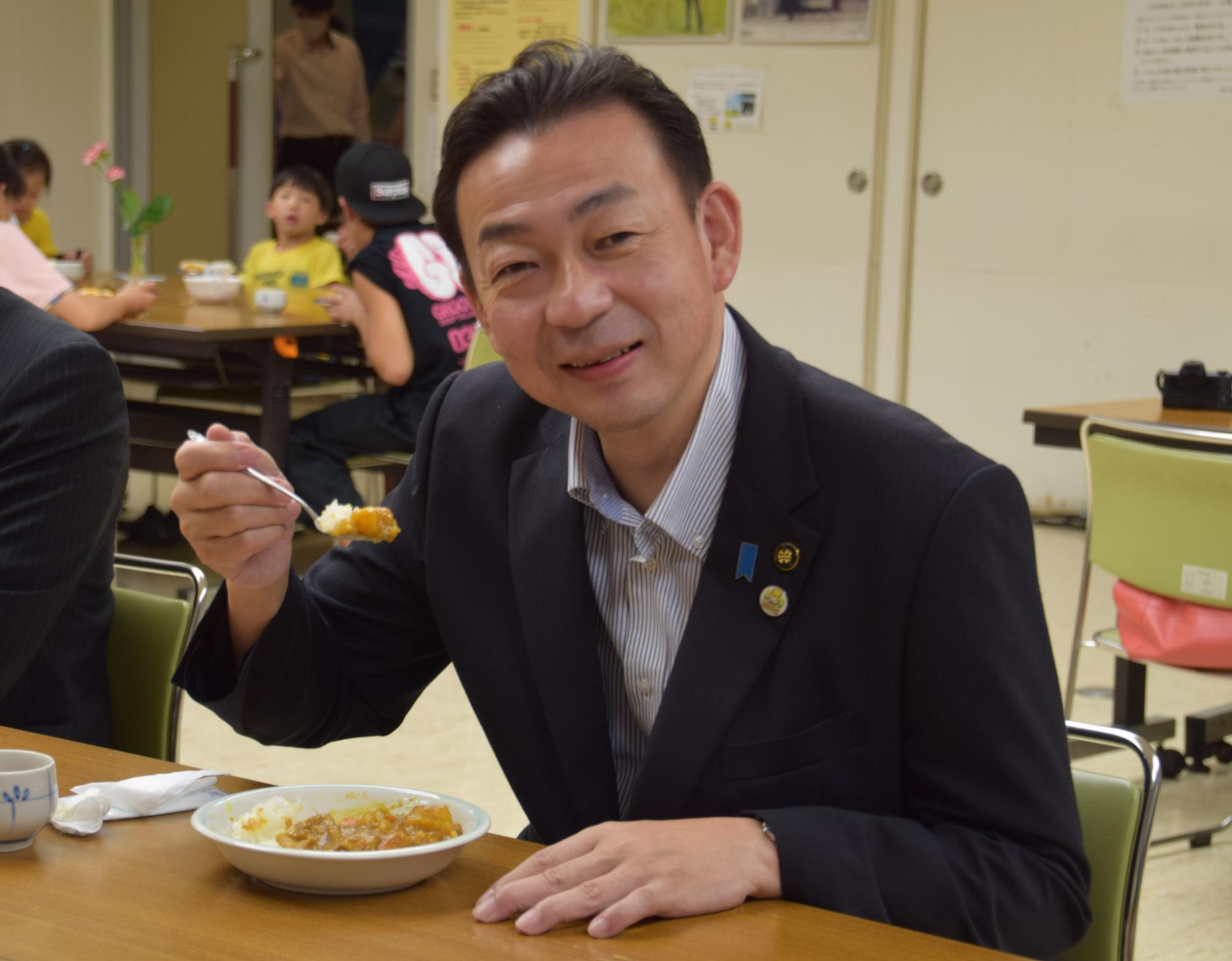 子ども食堂「おけがわ西口レストラン」で市長がカレーライスを食べている写真