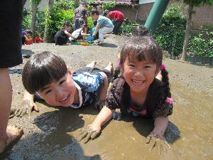 二人の子どもが泥んこの上で寝そべって笑っている写真