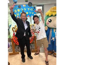 桶川市長とうどんYouTuberの武正倫さんが桶川栄養まつりの横断幕の前でガッツポーズをしている写真