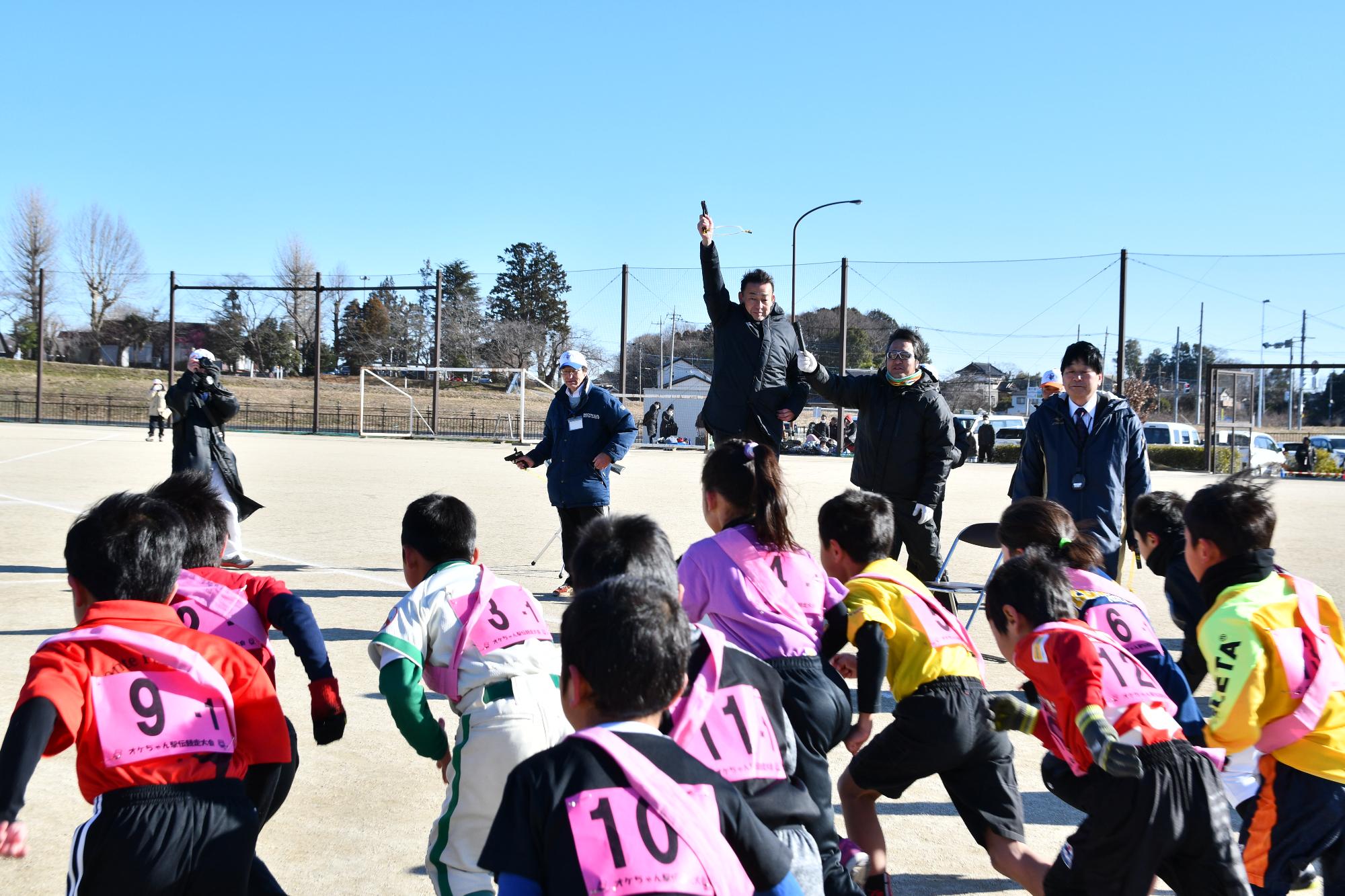 オケちゃん駅伝競走大会で、小学生1、2年生のスターターを務めた市長と、スタンバイする小学生が写っています