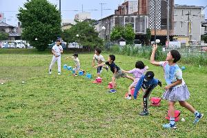 横一列に並んでボールを投げるこどもたちと見守るかじ川さんの写真
