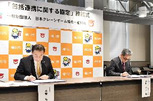 一般社団法人日本クレーンゲーム協会中村秀夫代表理事と桶川市長が協定書にサインしている写真