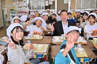 桶川市長と朝日小学校の生徒が給食を食べながら笑顔でピースをして映っている写真